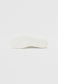Witte rubberen schoenenzool met een gestructureerd oppervlak met kleine cirkelvormige stippen en branding. Gebogen vorm met verhoogde randen voor grip.