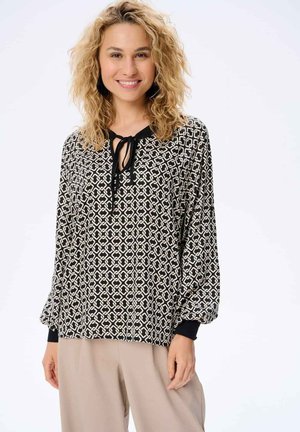 Schwarz-weiß gemusterte Bluse mit einem Bindegürtel am Hals, langen Ballonärmeln und einfarbigen schwarzen Manschetten. Leichte Stoffqualität mit abstraktem Design.