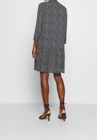 Black floral dress with three-quarter sleeves, a high collar, and a tiered skirt. Worn with black strappy heels and intricate ankle straps.