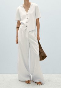 Valkoinen lyhythihainen V-puolelta oleva paita, jossa on nappikiinnitys, yhdistetty leveälahkeisiin valkoisiin housuihin. Asusteina ruskea käsilaukku ja litteät sandaalit.