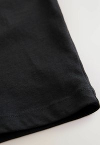  camiseta de algodón negra con un dobladillo de textura acanalada. Bordes redondeados y un acabado suave. Colocada plana sobre un fondo claro.