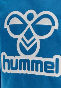 Blå sweatshirt med et stort hvidt logo med en stilisering af en bi og ordet "hummel" i afrundede bogstaver, præsenteret fremtrædende.