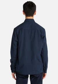 Donker marineblauw overhemd met lange mouwen, klassieke kraag en rechte zoom. Kenmerkt zich door een gladde katoenstructuur en meerknopmanchetten.