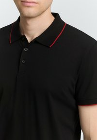 Mustmust särk krae ja punase aktsendiga kraes ja varrukatel. Sellel on nööbilehe ja sile tekstuur.
