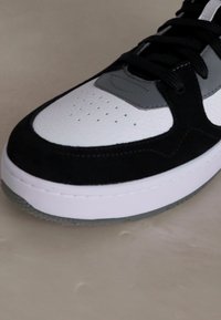 Black and white sneaker features a textured suede upper, smooth leather accents, and a thick white sole with grey details.