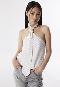 Top bianco a halter con righe navy, caratterizzato da un dettaglio annodato al collo. Abbinato a jeans grigi chiari decorati con piccoli ornamenti.