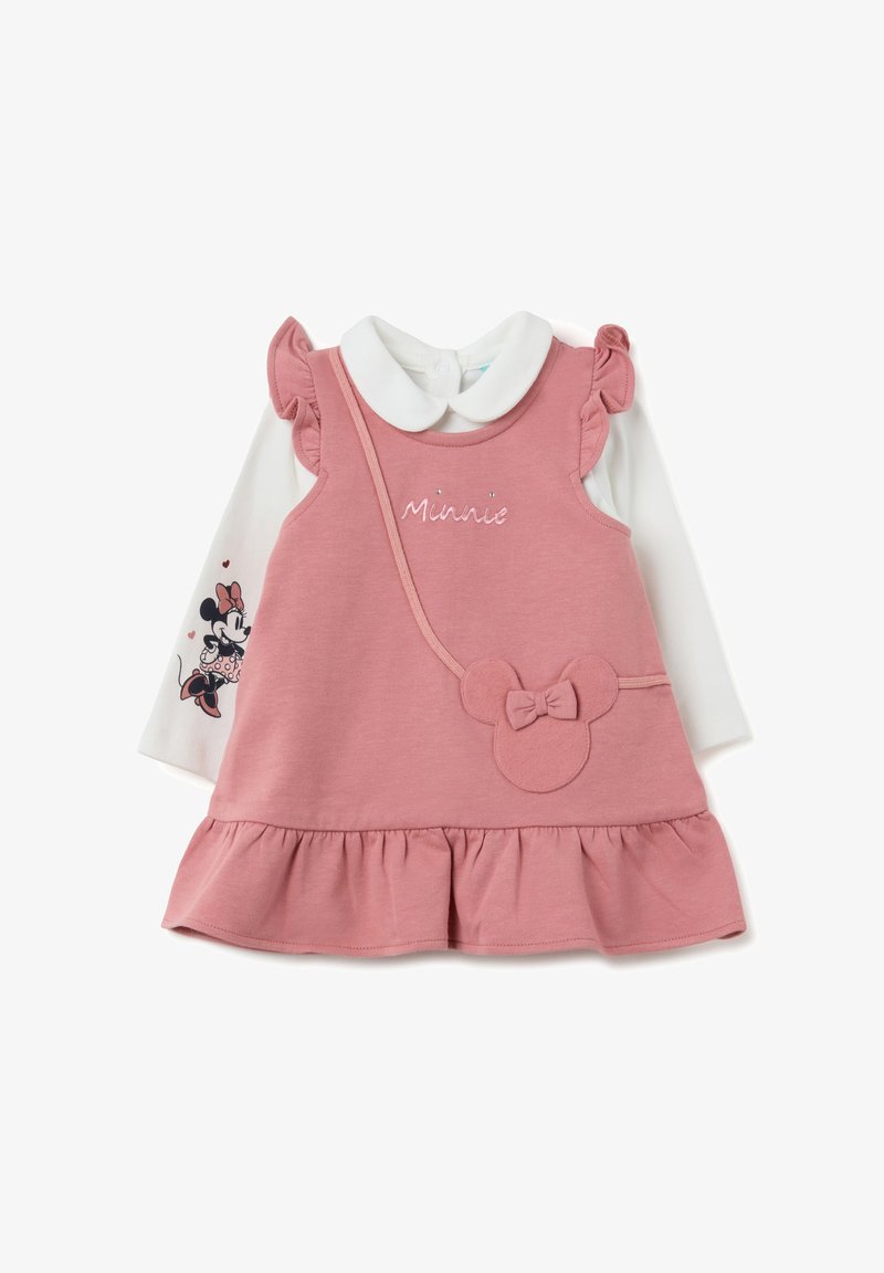 Robe sans manches rose avec des accents de fronces sur les épaules, dotée d'un col rond et d'un nœud décoratif. Superposée avec une chemise blanche à manches longues.