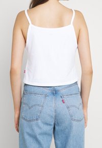 Vit kortärmad tanktopp med smala band, i kombination med ljusblå högmidjade jeans med två bakfickor och röd märkestagg.