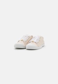 Sneakers in tela beige con lacci bianchi, caratterizzati da una texture rigata e suole in gomma bianca. Occhielli dorati nei fori per i lacci.