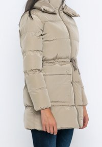 Beige Pufferjacke mit Kapuze, Reißverschluss, verstellbarem Bund und seitlichen Taschen. Sie verfügt über eine glatte, glänzende Textur und ein gestepptes Design.