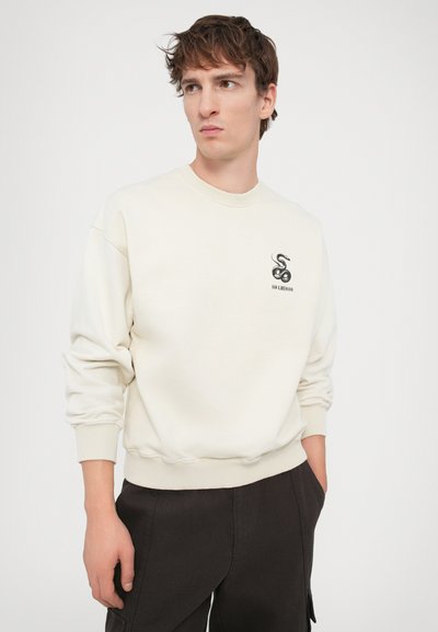 Lyscreme sweatshirt med ribbede manchetter og kant; har et sort slangesymbol på venstre bryst; blød tekstur, afslappet pasform.