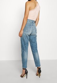 Světle růžový krajkový body spárovaný se světle modrými vybledlými džíny s vysokým pasem, se zúženými nohavicemi a černými sandály na vysokém podpatku.