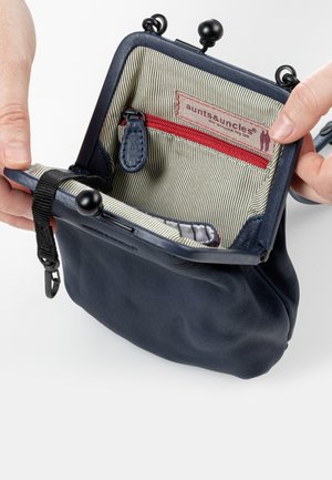 Granatowa skórzana torebka na ramię z zapięciem na klamrę i podszewką w paski. Posiada czerwoną kieszeń na zamek oraz metkę z logo wewnątrz. Miękka w dotyku.