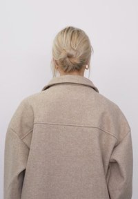 Beež oversize villane mantel pehme tekstuuriga, laia krae ja allapoole laskuvate õlgadega. Seljaosa on varustatud lihtsa õmbluse detailiga.