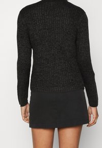 Schwarzer gestrickter Pullover mit strukturiertem Muster, langen Ärmeln und rundem Ausschnitt, kombiniert mit einem schwarzen Rock, Ansicht von hinten.