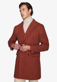 Dobbeltbrystet frakke i rustfarvet stof med struktureret finish, udstyret med sorte knapper, klippede rever og sidelommer.