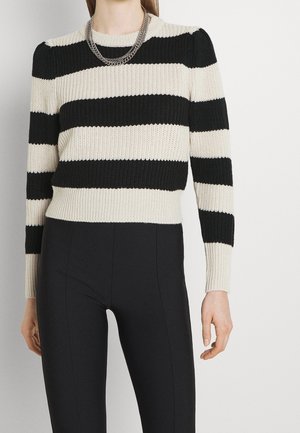 Pull à rayures noir et crème avec une texture côtelée, encolure ronde et manches longues. Porté avec un pantalon noir ajusté et une chaîne en argent à plusieurs couches.