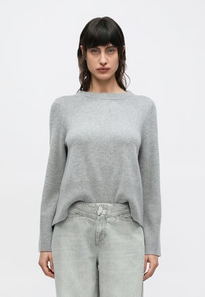 Světlé šedý pletený svetr s dlouhými rukávy a kulatým výstřihem, s žebrovaným lemem a volnějším střihem. Kombinován se světlými šedými džínami.