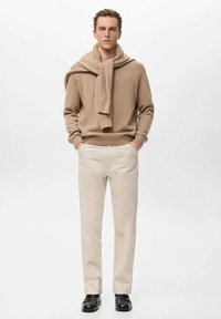 Jersey beige claro con cuello redondo y puños remangados, combinado con una bufanda a juego. Combina con pantalones color crema y zapatos negros.