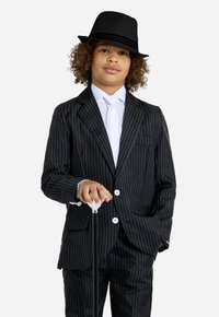 Completo a righe nere con bottoni bianchi, camicia bianca e cravatta. Un cappello a falda nera e un bastone con manico bianco completano l'insieme.