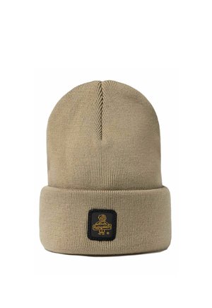 Berretto beige lavorato a maglia con risvolto, caratterizzato da una patch nera con un cane giallo e testo sul davanti, esposto su sfondo bianco.