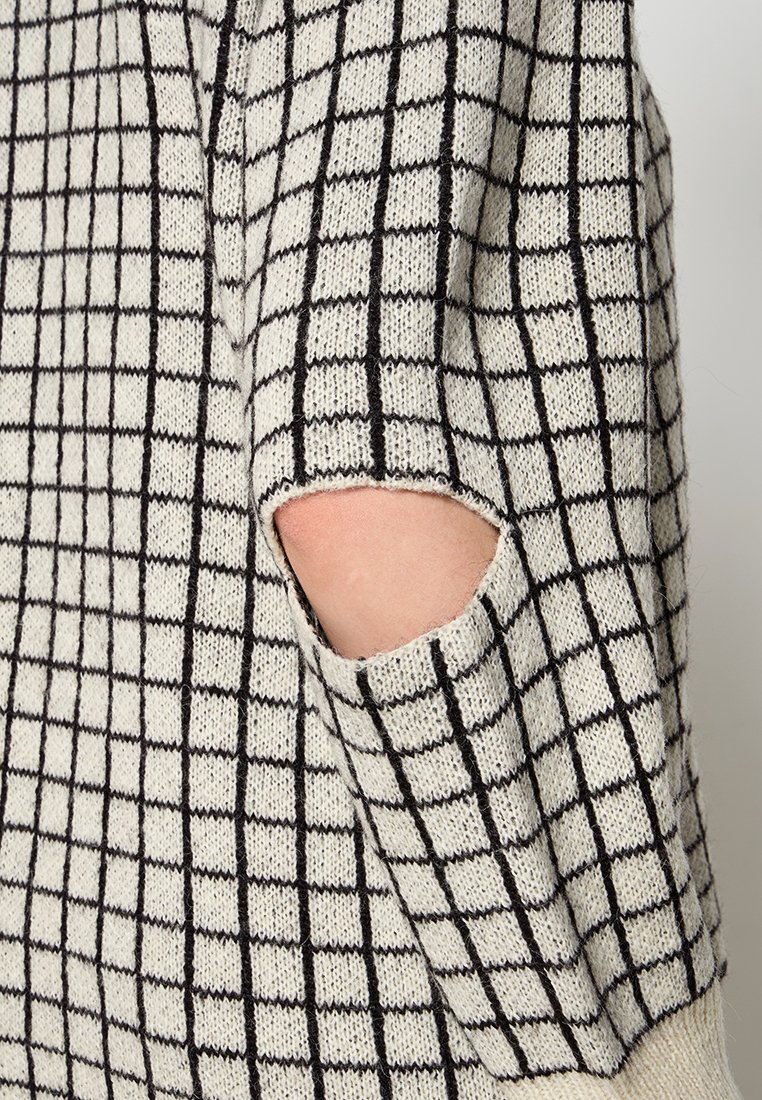 Sweter dzianinowy w czarno-białym wzorze w kratę. Posiada wycięcie na łokciu oraz miękką teksturę, podkreślając kontrastujące kolory.