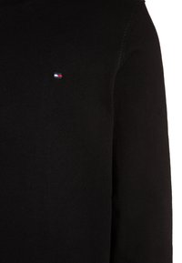 Black sweater with a round neckline, made of soft knit fabric. Features a small embroidered logo in red, white, and blue on the chest.