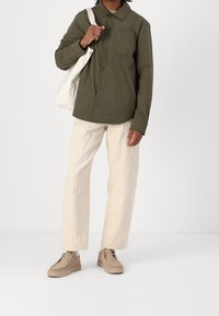 Olivengrøn skjorte med knapper og en brystlomme, kombineret med off-white bukser med lige ben og beige slip-on sko. En hvid tote-taske holdes.