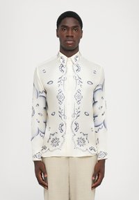 Hemd aus creamfarbener Seide mit blauen Blumenmustern und geschwungenen Akzenten. Verfügt über einen klassischen Kragen und lange Ärmel.