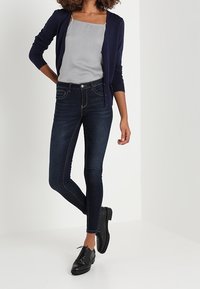 Laivasto cardigan, harmaa toppi, tummat skinny-farkut ja mustat nauhalaukkukengät. Sujuva kangas, istuva muotoilu ja hienovaraiset ompeluyksityiskohdat.
