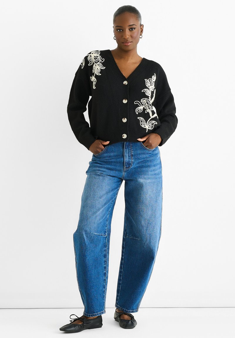 Black cardigan with floral embroidery, v-neck, five-button closure, paired with high-waisted blue jeans and black ballet flats.