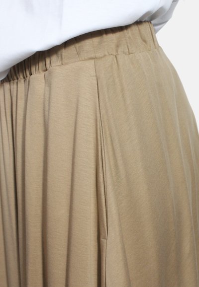 Gonna a pieghe beige con cintura elastica. Realizzata in un tessuto morbido, presenta pieghe verticali e una texture soffice. Il design è di lunghezza media.