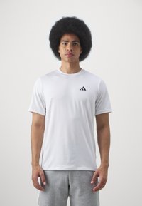 T-shirt de sport blanc à manches courtes avec un logo Adidas noir sur la poitrine gauche. Texture lisse, tissu léger, design ajusté.
