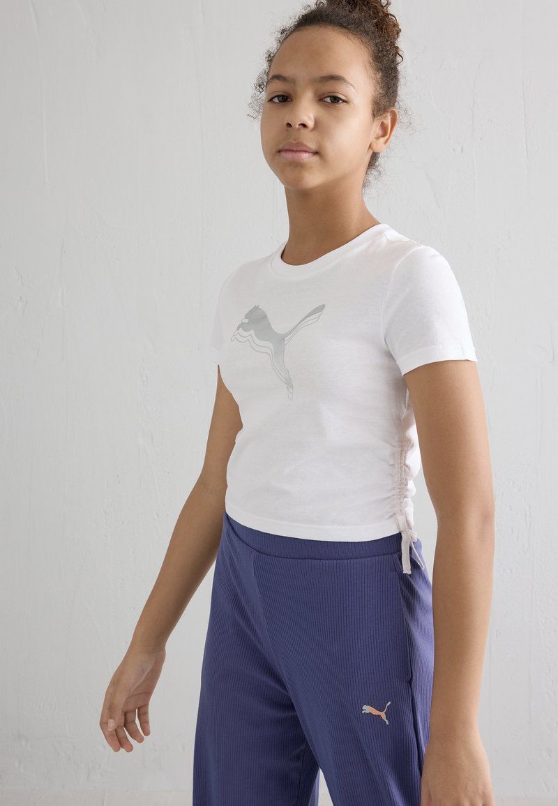 Valge lühikese varrukaga T-särk heleda halli Puma logoga, külgsete rüüsidega detailiga. Kombineeritud tumesiniste ribadega pükstega, sisaldab väikest logo.