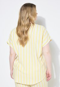 Haut à manches courtes rayé jaune et blanc avec une coupe décontractée, un ourlet arrondi et une texture douce, vu de l'arrière.