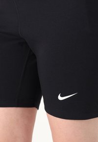 Schwarze sportliche Shorts aus dehnbarem Material, mit einem taillierten Design und einem weißen Nike-Logo auf der unteren rechten Seite.