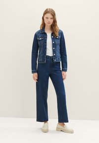 Dark blue denim jacket with front pockets, white T-shirt underneath, paired with wide-leg dark blue jeans and cream loafers.