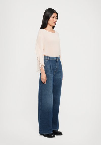 Helles pinkes Blusenshirt mit Rüschensäumen, kombiniert mit hoch taillierten, weit geschnittenen, dunkelblauen Jeans und schwarzen Schuhen. Einfaches Design und Struktur.