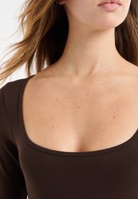 Braunes, geripptes Langarmoberteil mit weitem Ausschnitt und glatter Textur, das die Form durch einen figurbetonten Schnitt betont.