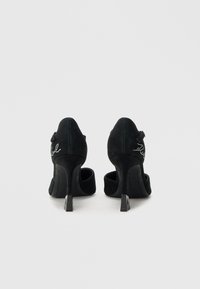 Μαύρα σουέντ ψηλοτάκουνα παπούτσια με στρογγυλερή μύτη, κλείσιμο με αγκράφα στο πίσω μέρος και διακοσμητικά στρας στην εξωτερική πλευρά. Υφή με ανάγλυφη αίσθηση.