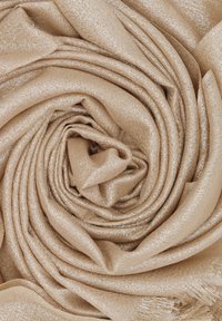 Sciarpa beige con una texture morbida e scintillante, arrotolata ordinatamente a spirale. Il materiale presenta accenti metallici intrecciati.