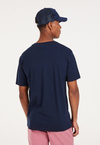 Camiseta azul marino de manga corta, hecha de una tela ligera. La vista posterior muestra un ajuste relajado y un escote redondeado.