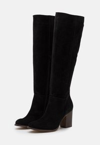 Botas de ante negras hasta la rodilla con tacón cuadrado, que cuentan con una cremallera lateral y una textura suave. Punta redondeada y silueta estructurada.