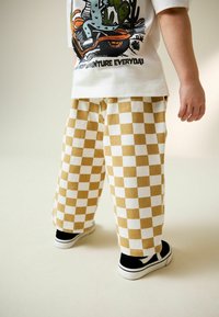 Pantalones de cuadros en beige y blanco con un corte relajado, combinados con zapatillas en blanco y negro, presentando una textura suave y detalles de costura visibles.