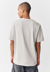 Vaaleanharmaa puuvillainen T-paita, jossa on lyhyet hihat, pyöreä pääntie ja rento istuvuus, sileä pinta ei sisällä näkyviä kuvioita tai grafiikkaa.