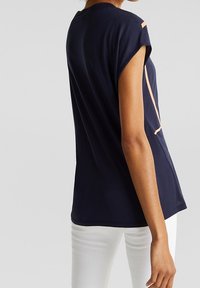 Mörkblå t-shirt med korta uppvikta ärmar, försedd med en kontrasterande ljusorange detalj på sidan. Mjuk, slät tygkänsla och avslappnad passform.