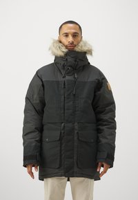 Sort parka-jakke med pelsforet hætte, frontlynlås, snoretræk og to frontlommer. Lavet af tekstureret, vejrbestandigt materiale.