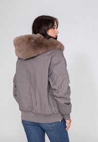 Graue Bomberjacke mit einem mit Fell gefütterten Kapuze, gerippten Bündchen und Saum. Glattes Material mit einer entspannten Passform und seitlichen Reißverschlusstaschen.