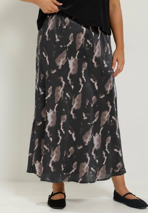 Donna che indossa una lunga gonna con motivo astratto nero e grigio, scarpe nere basse e un top nero parzialmente visibile.