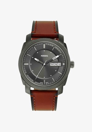 Ronde zwarte Fossil polshorloge met gestructureerde lunette, bruine leren band, witte uurmarkeringen en dag-datumweergave die maandag 18 toont.